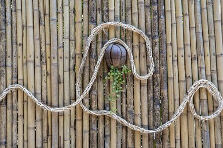 Decorated bamboo wall with a rope and a coconut flower pot on a tropical beach in paradise island...