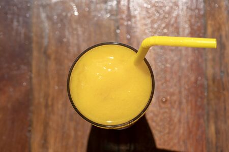 Mango smoothie in a glass on wooden background. Yellow mango shake. Tropical fruit concept. Top view, close upの写真素材