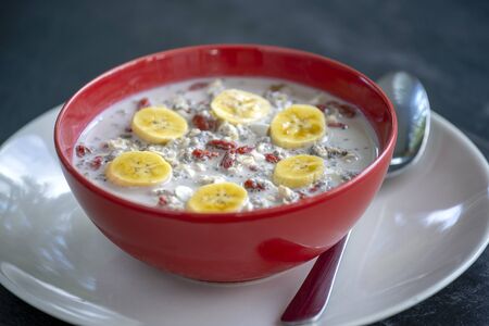 Fresh breakfast of granola, yogurt, nuts, goji berries, chia seeds and banana. Muesli with fruits and berries in red bowl, close upの写真素材