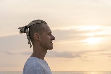 Silhouette of a young guy with dreadlocks on his head near sea during sunset. Close up portrait....