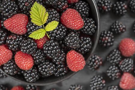 Background from fresh organic blackberries and raspberries, close up. Lot of ripe juicy wild fruit raw berries in a black plate. Top view blackberry and raspberryの写真素材