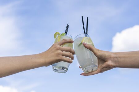 Two girls holding mojito cocktail in the hand against the blue sky. Freshness cocktail, close up