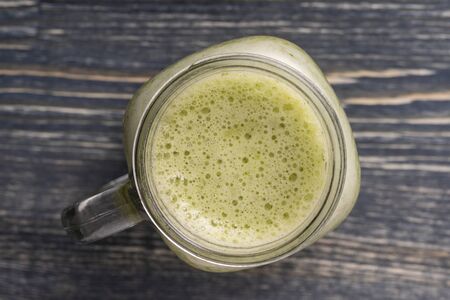 Fresh green smoothie from avocado, kiwi, banana, honey, dill and parsley in glass mug on wooden background, close up, top view. Concept of healthy eatingの写真素材