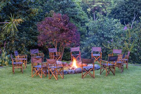 View of the burning bonfire together around it with chairs on the green lawn near the forest, Tanzania, East Africaの写真素材