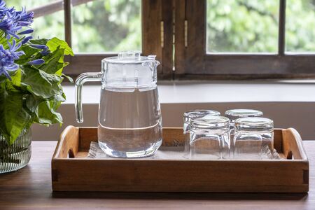 A carafe of water and four empty glasses on a wooden tray next to the window, close upの写真素材