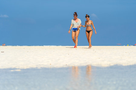 Zanzibar, Tanzania - january 03, 2020 : Two girls in swimsuits go to the ocean on the tropical sand beach of Zanzibar island, Tanzania, East Africaのeditorial素材