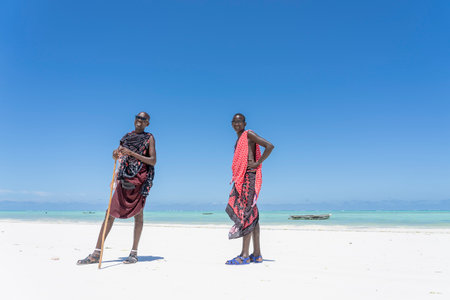 Zanzibar, Tanzania - october 28, 2019 : Two african men masai dressed in traditional clothes standing near the ocean on the sand beach, Zanzibar, Tanzaniaのeditorial素材