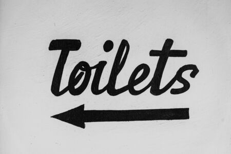Black inscription toilets on a white wall with a pointer, close up