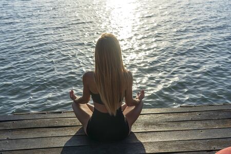 Silhouette of woman sitting at yoga pose on the tropical beach during sunset. Caucasian girl...