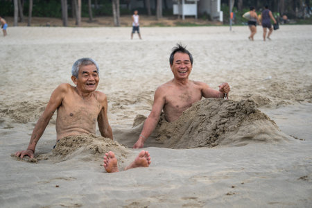 Danang, Vietnam - june 15, 2020 : Two vietnames men taking a bath of beach sand for therapy near sea water in the morning on the city Danang, Vietnam. Local people relax on the beachのeditorial素材