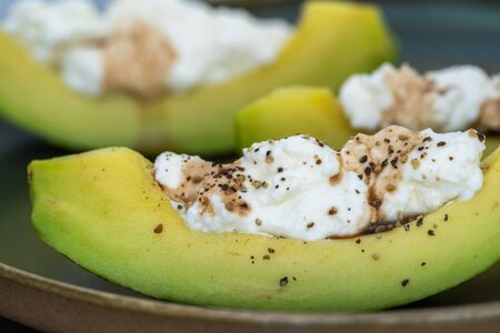 Fresh green sliced avocado with white cream cheese and pepper on a plate, close up. Healthy eating...