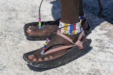 Tribal masai legs with a colorful bracelet and sandals made of car tires on the sand beach, close up. Island of Zanzibar, Tanzania, East Africaの写真素材