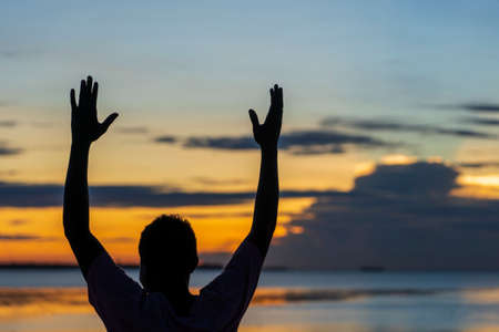 Silhouette of a happy african guy with hands up during sunset by the ocean on the island of Zanzibar, Tanzania, East Africa, close upの写真素材