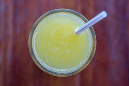Glass of orange juice with drinking straw on wooden background, top view, close up