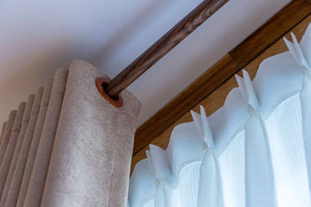 Window beige curtains and white tulle on the curtain rod, close upの写真素材