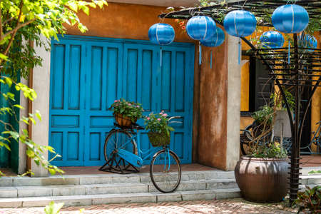 Vintage bike with basket full of flowers next to an old building in Danang, Vietnam, close up. Bicycle with a basket of flowers against the backdrop of an obsolete wallの写真素材