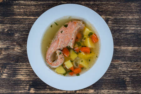 Fresh salmon fish soup with carrots, potatoes and herbs in a white plate, close up. Tasty dinner consists of a fish soup with salmonの写真素材
