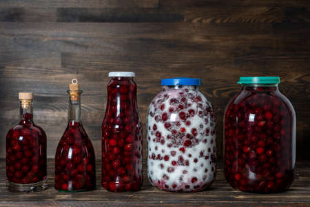 Homemade tincture of red cherry. Berry alcoholic drinks concept. Homemade red wine made from ripe cherries in glass bottles and jars on wooden background, Ukraineの写真素材