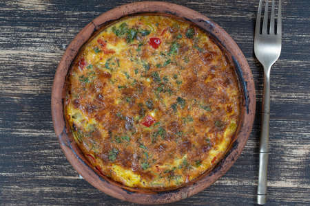 Ceramic bowl with vegetable frittata, simple vegetarian food. Frittata with tomato, pepper, onion and cheese on wooden table, close up. Italian egg omelette, top viewの写真素材