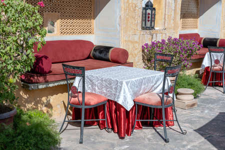 Street cafe in old town, outside in Jaipur, Rajasthan, India. Table, sofa and chairs near old wall,...