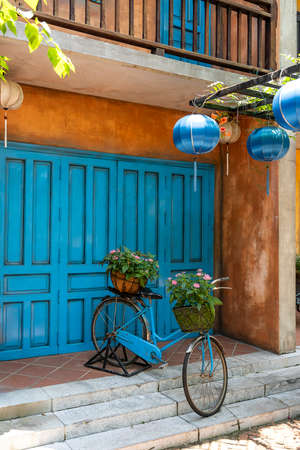 Vintage bike with basket full of flowers next to an old building in Danang, Vietnam, close up. Bicycle with a basket of flowers against the backdrop of an obsolete wallの写真素材