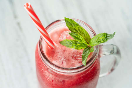 Fresh organic red smoothie in glass mug on white table, close up. Refreshing summer fruit drink. The...