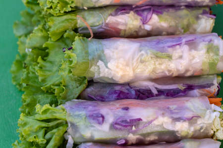 Wrapped rice noodles, green lettuce leaf, carrot and blue cabbage, close up. Fresh rolls with rice...