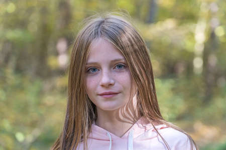 Pretty young blonde girl with freckles on the autumn landscape, closeup portrait