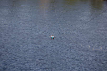 Rear view of young man riding on zip line against a background of a blue river water wave, Kyiv,...