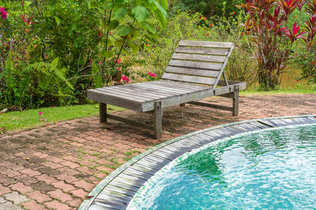 Wooden deck chair for relaxing by the pool in tropical garden, Malaysia