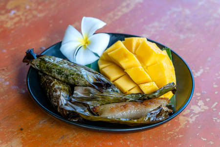 Thai style dessert, yellow mango with banana sticky rice in palm leaves. Yellow mango and sticky rice is popular traditional dessert of Thailand. Close upの写真素材
