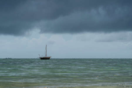 Traditional fisherman dhow boat and stormy sky during sunset on Indian ocean in island Zanzibar,...
