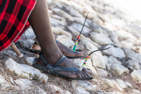 Tribal masai legs with a colorful bracelet and sandals made of car tires on the sand beach, close...