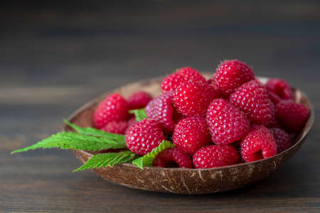 Harvest of ripe farm red raspberries in coconut plate on the table, on brown wooden background....