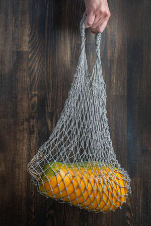 Female hand hold reusable mesh bag with pumpkin on wooden background, close up