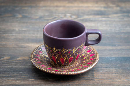 Decorative ceramic painted cup and saucer on wooden background, close up. Decorative porcelain cup and saucer painted with acrylic paints, handwork, dot paintingの写真素材