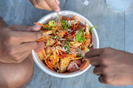 Three male hands with forks eat thai vegetable salad along with sausages, top view, close up