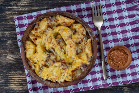 Baked potato, onion and garlic with cheese on the wooden table, close up. Ceramic bowl with potato...