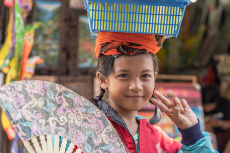 UBUD, BALI, INDONESIA - MARCH 01, 2019: Young Indonesian girl selling decorated hand fans for...