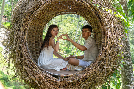 UBUD, BALI, INDONESIA - MARCH 11, 2019: Asian woman and man enjoying his time sitting on bird nest in tropical jungle near the rice terraces in island Bali, Indonesia. Nature and travel conceptのeditorial素材