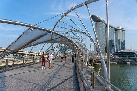 SINGAPORE CITY, SINGAPORE - MARCH 29, 2019: Tourists walk on helix bridge with Marina Bay Sands in background. Tourism in Singapore is major industry and contributor to its economyのeditorial素材
