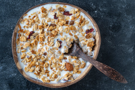 Granola with oatmeal, dried fruit, honey, raisins, dry cranberry, almond and cashew nuts with yogurt in a coconut bowl, close up, top view. Healthy breakfast conceptの写真素材