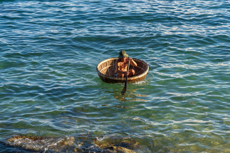 Cu Lao Cham, Vietnam - June 11, 2020: Vietnamese fisherman in a traditional round woven bamboo boat rowing to makeshift living rafts on open sea of Cu Lao Cham island near Danang, Vietnamのeditorial素材