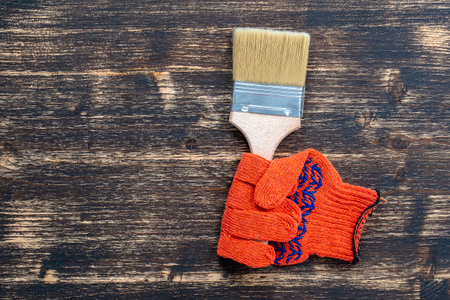 Orange construction gloves in which the paint brush is clamped. Surface painting. Means of protection. Tool kit, paint brush and work gloves on wooden background, top view, copy space for textの写真素材