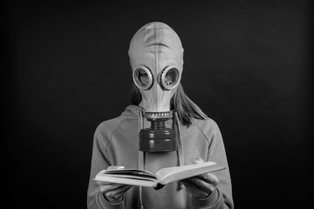 Girl in a gas mask reads a book on a black background, close up, black and whiteの写真素材