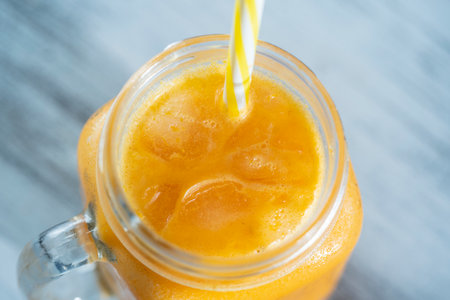 Fresh organic yellow smoothie in glass mug on white wooden table, close up. Refreshing summer fruit drink. The concept of healthy eating. Sea buckthorn with honey and water smoothie in sunny dayの写真素材