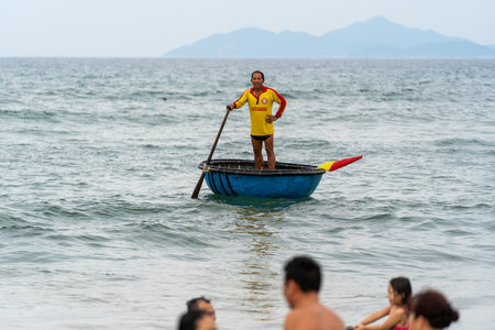 Danang, Vietnam - June 14, 2020: Vietnamese marine lifeguard in a traditional round woven bamboo boat watches people swimming in the permitted area on the city Danang, Vietnamのeditorial素材