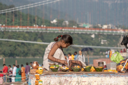 RISHIKESH, INDIA - NOVEMBER 06, 2018: A young girl makes baskets with flowers for the sale of...