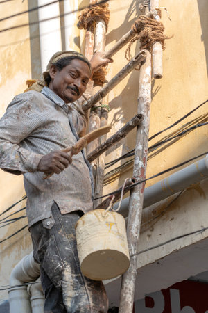 RISHIKESH, INDIA - NOVEMBER 06, 2018: Happy Indian man paints the wall at home with a tassel standing on the wooden stair in Rishikesh, India, close upのeditorial素材