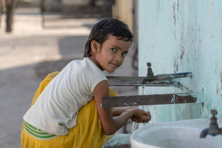 RISHIKESH, INDIA - NOVEMBER 06, 2018: Portrait of thirsty Indian girl drinks water from the outdoor tap on the street in Rishikesh, Indiaのeditorial素材